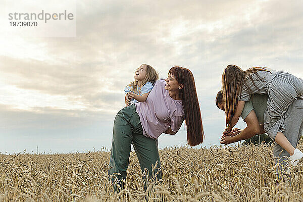Lächelnde Eltern und Töchter  die sich im Feld unter freiem Himmel amüsieren