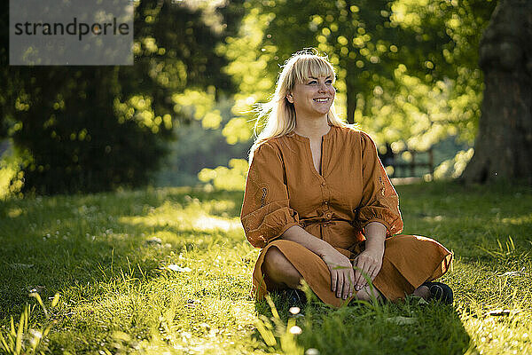 Glückliche blonde Frau sitzt auf Gras im Park