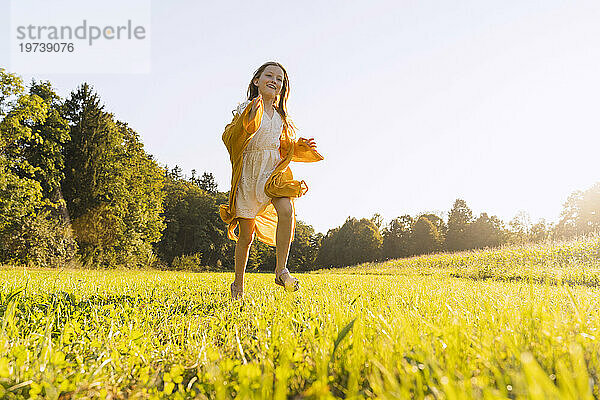 Cheerful girl running on grass in field