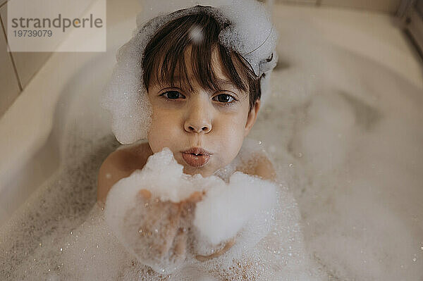 Cute boy blowing soap sud in bathroom at home