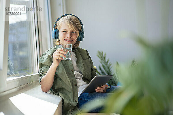 Lächelnder Junge mit Glas Wasser und Tablet-PC zu Hause