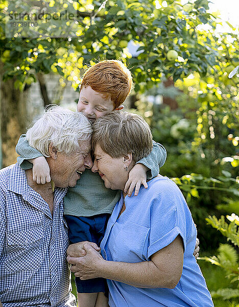 Junge mit den Armen um Großeltern im Garten