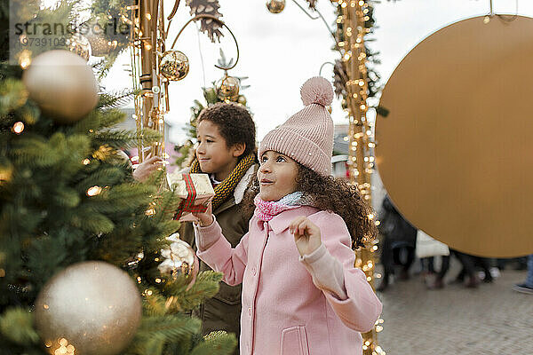 Glückliches Mädchen hält Geschenkbox in der Hand und genießt mit Bruder auf dem Weihnachtsmarkt
