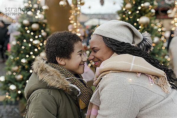 Lächelnde Mutter reibt ihrem Sohn auf dem Weihnachtsmarkt die Nase