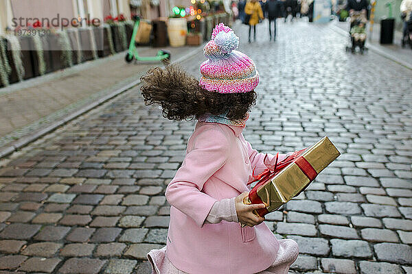 Glückliches Mädchen hält Geschenkbox in der Hand und rennt auf der Straße