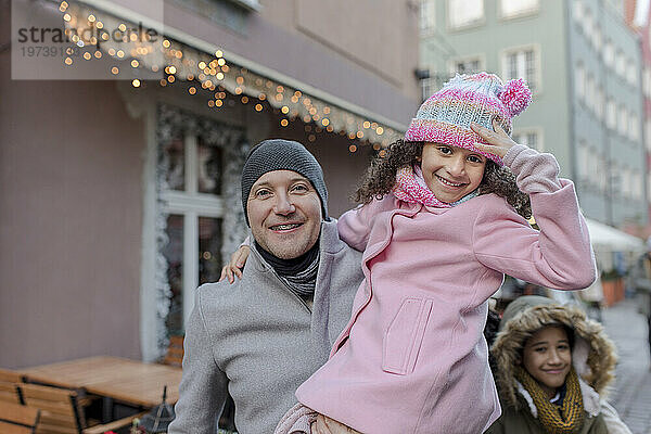 Lächelndes Mädchen mit Vater und Bruder auf dem Weihnachtsmarkt