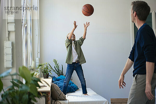 Vater und glücklicher Sohn spielen zu Hause Basketball