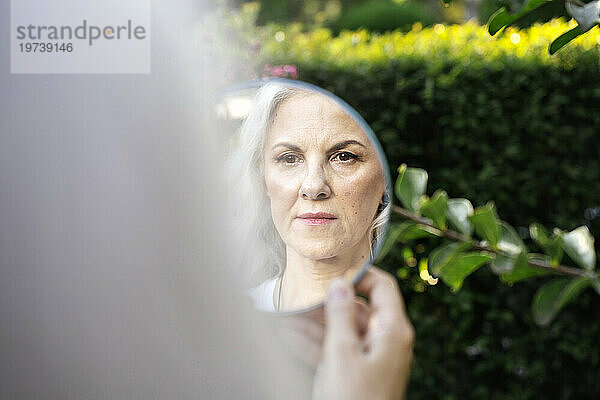 Reife Frau mit grauem Haar blickt auf das Spiegelbild