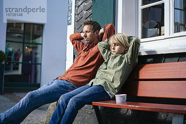 Father and son with hands behind head sitting on bench