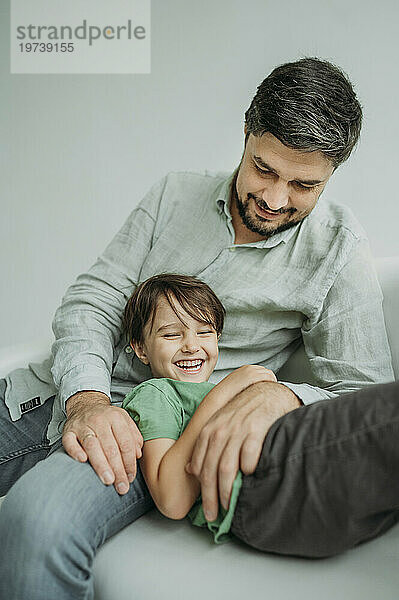 Glücklicher Mann mit Sohn  der auf dem Sofa vor weißem Hintergrund liegt