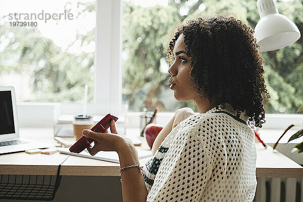 Curly haired teenage girl talking on smart phone at desk near window