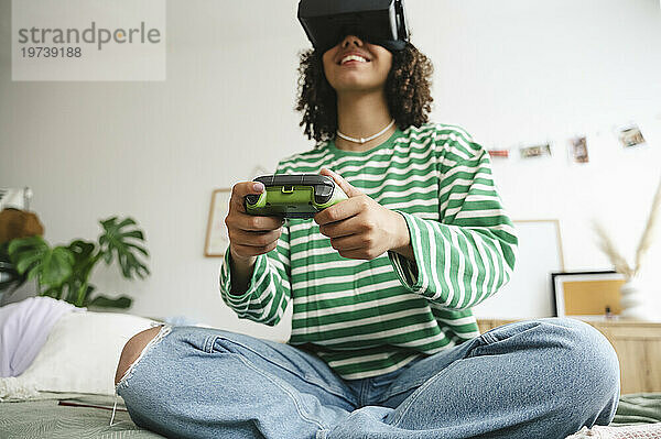Happy girl wearing virtual reality simulators playing video game with controller in bedroom
