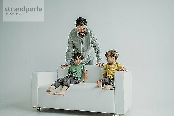 Happy children sitting on sofa with father standing against white background