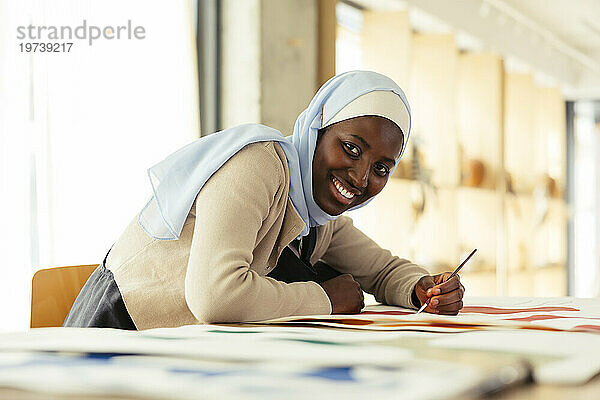 Smiling artist wearing headscarf painting with brush in studio