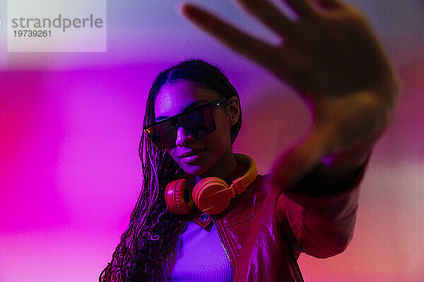 Young woman with headphones and sunglasses gesturing in illuminated tunnel