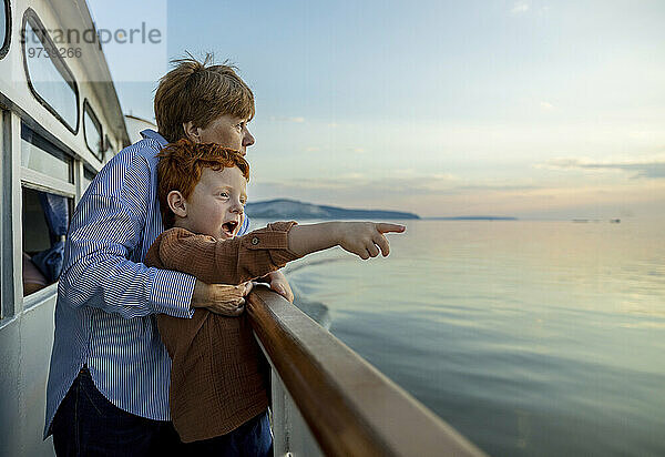 Netter Junge gestikuliert in Richtung Meer  während Großmutter in der Abenddämmerung auf dem Schiff genießt