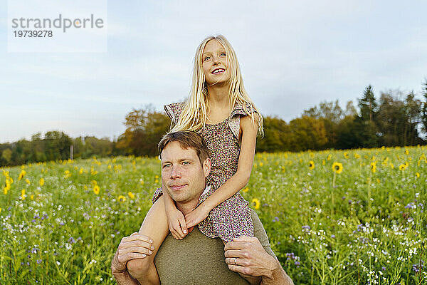 Smiling father carrying daughter on shoulders in field
