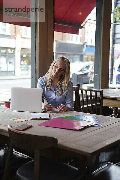 Blonder Freiberufler macht sich im Café Notizen vom Laptop