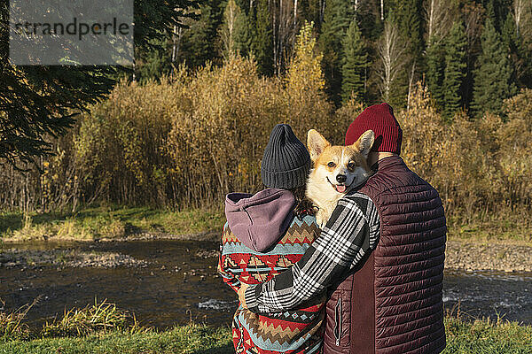 Paar umarmt am Wochenende Corgi-Hund am Flussufer im Park