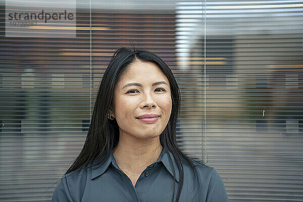 Lächelnde Geschäftsfrau mit schwarzen Haaren vor Glas