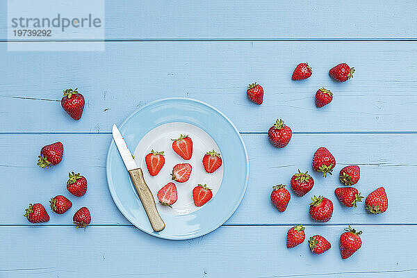 Teller  Küchenmesser und reife Erdbeeren auf blauer Holzoberfläche