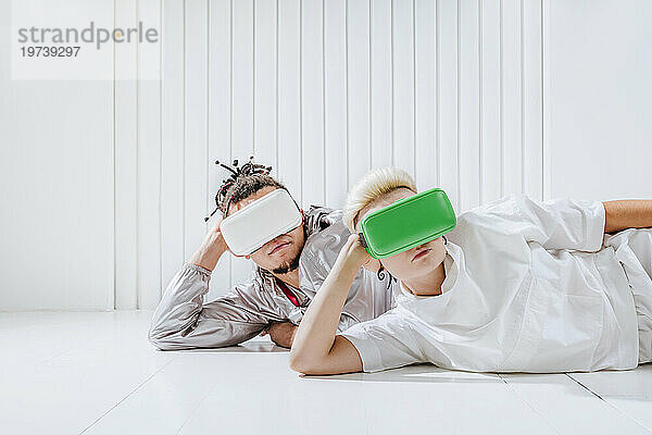 Mann und Frau mit Virtual-Reality-Headset liegen auf der Seite vor einer weißen Wand
