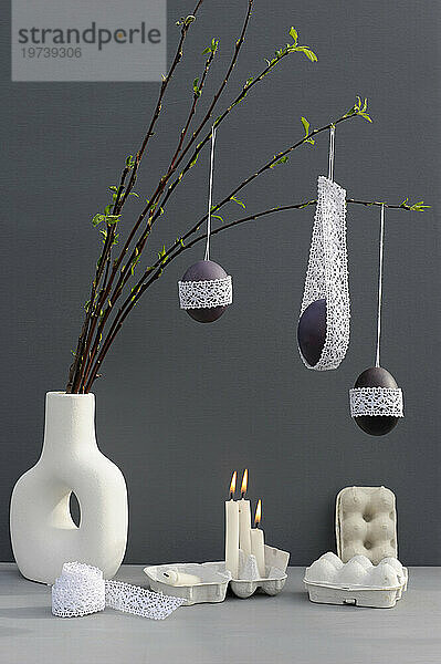 Studio shot of candles burning under laced Easter eggs hanging from twigs in vase