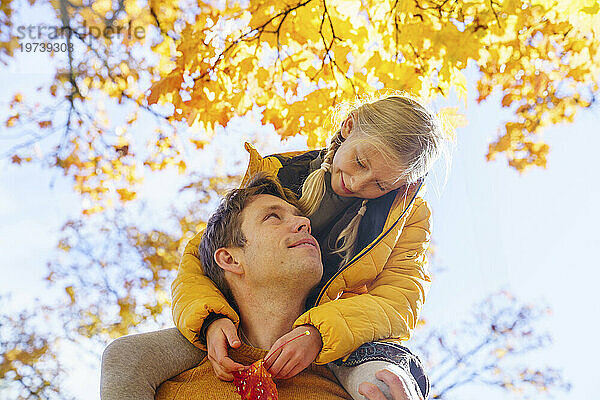 Liebevoller Vater trägt Tochter auf Schultern unter Baum