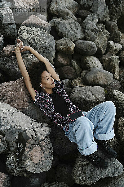 Junge Frau mit erhobenen Armen entspannt sich auf Felsen