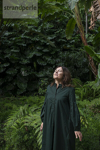 Reife Frau mit geschlossenen Augen steht im Botanischen Garten