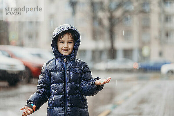 Lächelnder Junge genießt den Regen auf der Straße