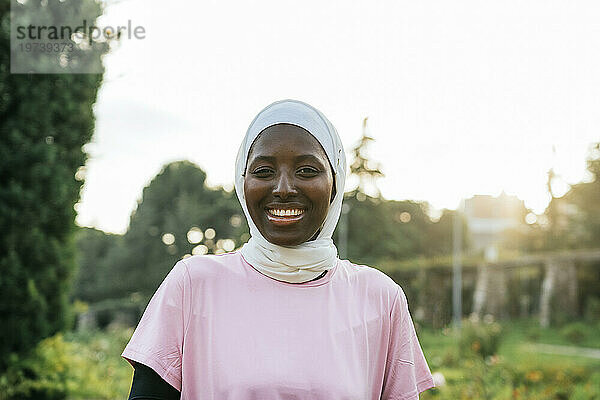 Smiling young woman wearing hijab in park at sunset