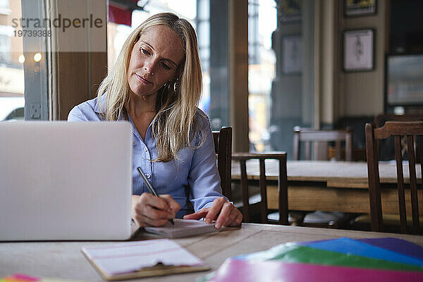 Blonder Freiberufler macht sich Notizen vom Laptop im Café