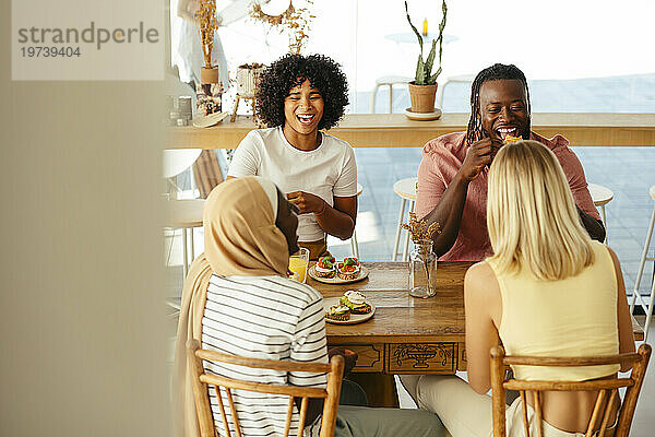 Lächelnde Freunde essen Bruschetta und Orangensaft am Tisch im Café