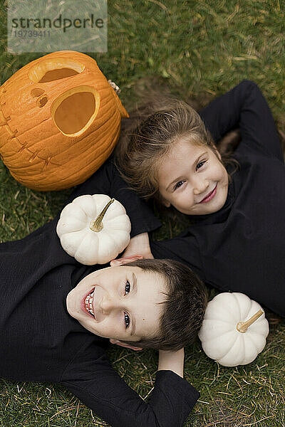 Junge und Mädchen liegen zu Halloween im Gras neben Kürbissen
