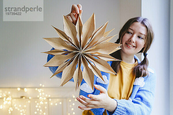 Happy teenage girl holding star shaped Christmas decoration at home