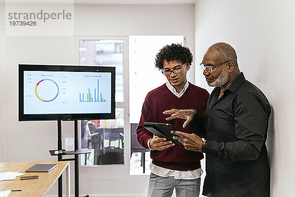 Reifer Geschäftsmann teilt Tablet-PC mit Kollegen im Konferenzraum am Arbeitsplatz