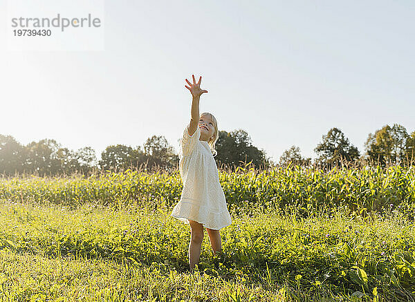 Happy girl with arm raised standing in meadow on a sunny day
