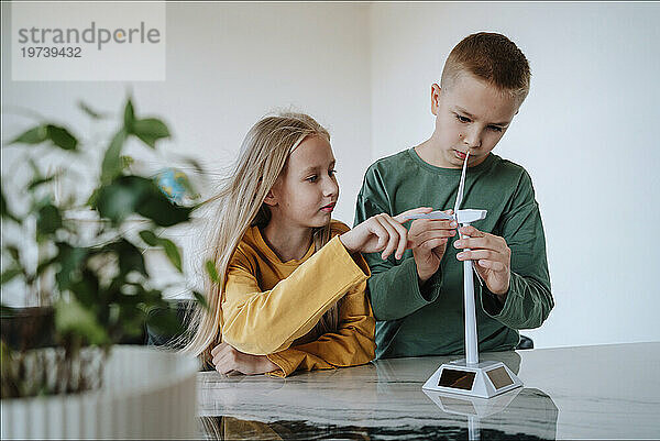 Bruder und Schwester berühren das Modell einer Windkraftanlage auf dem Tisch zu Hause