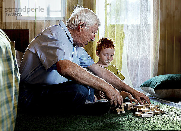 Älterer Mann und Enkel spielen zu Hause Blockentfernungsspiel