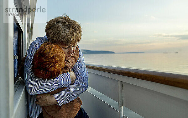 Liebevolle ältere Frau umarmt Enkel auf Schiff in der Abenddämmerung
