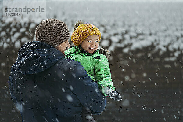 Fröhlicher Junge  der im Winter mit seinem Vater das verschneite Wetter genießt