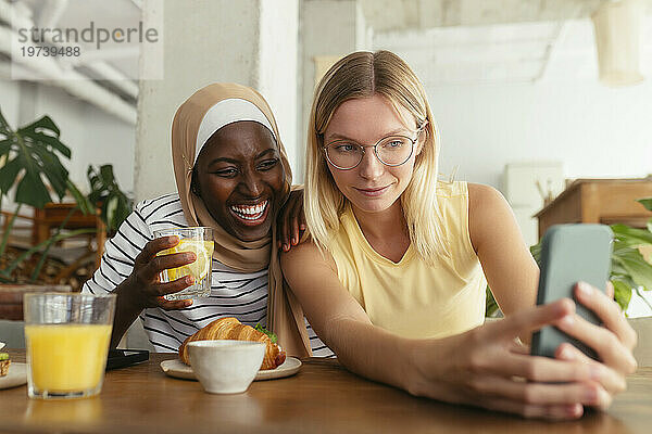 Lächelnde Freunde machen Selfie mit Essen auf dem Tisch im Café