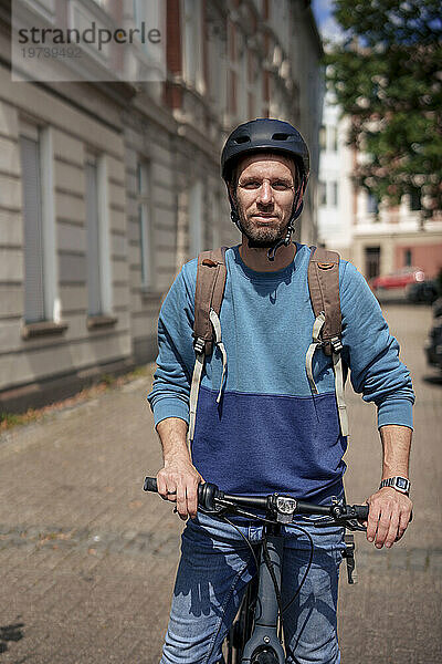 Lächelnder Mann mit Helm steht an einem sonnigen Tag mit dem Fahrrad