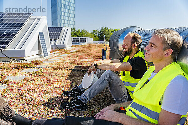 Zwei Techniker genießen eine Pause auf dem Dach eines Firmengebäudes  umgeben von Sonnenkollektoren