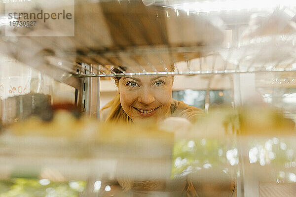 Lächelnder Besitzer  gesehen durch den Kühlschrank in der Bäckerei