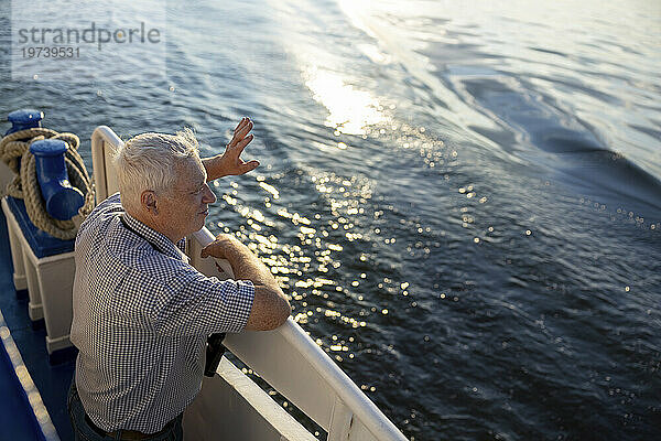 Älterer Mann steht am Geländer und winkt mit der Hand am Meer