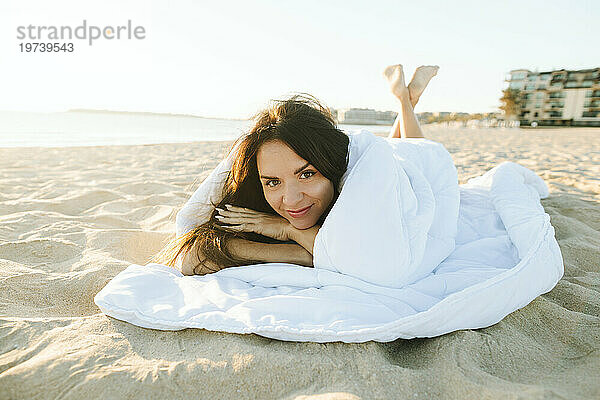 Smiling woman wrapped in blanket lying at beach