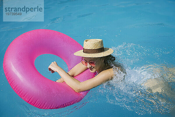 Frau mit Sonnenbrille schwimmt mit aufblasbarem Schwimmring im Pool