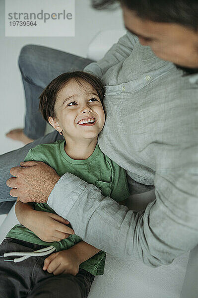 Lächelnder Junge liegt auf dem Schoß seines Vaters auf dem Sofa